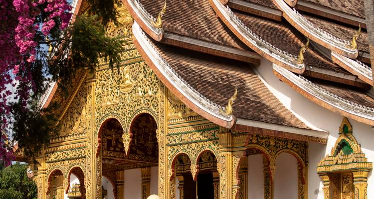 Elaborately carved entrance of a Lao temple with shimmering gold relief and sloping roofs.