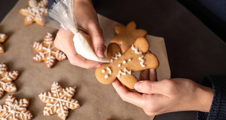 Des mains décorent un biscuit bonhomme en pain d'épices avec du glaçage blanc aux côtés de biscuits flocons de neige.
