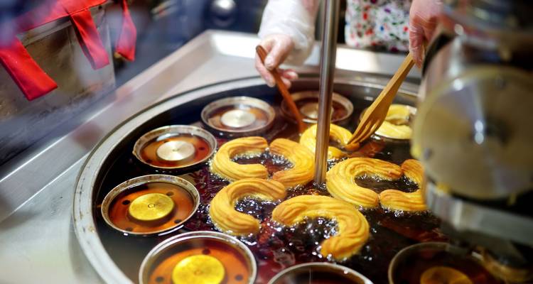 Des churros frais qui frient dans l'huile chaude tandis qu'un vendeur utilise des fourchettes en bois pour manipuler les anneaux de pâte.