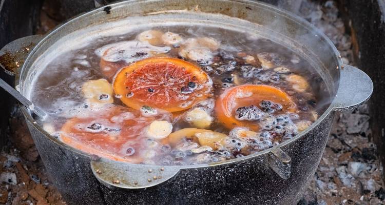 Chaudron en métal frémissant une boisson aux fruits et épices avec des tranches d'orange sur des braises incandescentes.