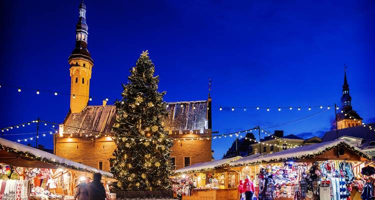 Place de la Vieille Ville de Tallinn la nuit avec un grand sapin de Noël décoré et des stands de marché sous des guirlandes lumineuses.