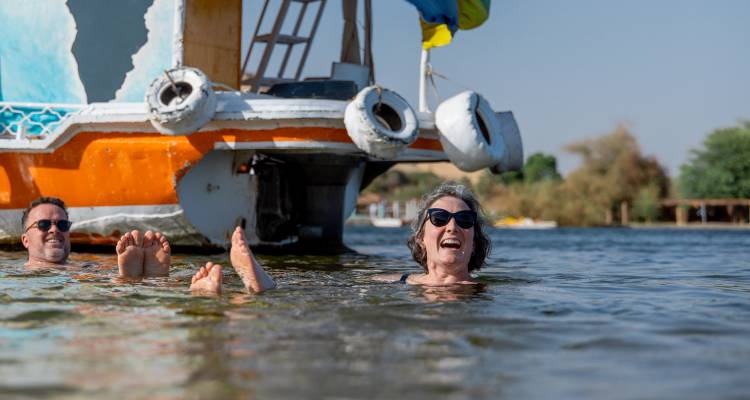 Des voyageurs souriants flottant sur le Nil à côté d'une barque traditionnelle colorée par une journée ensoleillée.