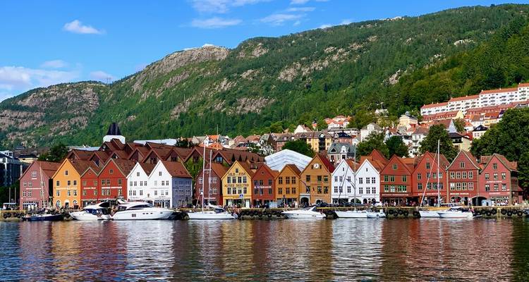 Los almacenes de madera colorida de Bryggen bordean el frente marítimo de Bergen, respaldados por montañas verdes y reflejados en aguas tranquilas.