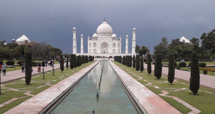 Klassiek frontaal zicht op het Taj Mahal dat weerspiegeld wordt in het lange marmeren bassin onder een dramatische bewolkte hemel.