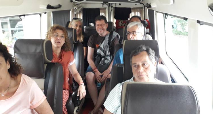 Kleine groep toeristen zit in een minibus, sommigen lachen en praten met elkaar terwijl anderen uit het raam kijken.