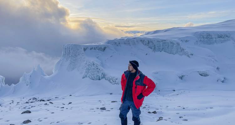 Alpinista con chaqueta roja de pie en las laderas nevadas con formaciones de hielo dramáticas y nubes en el Monte Kilimanjaro.