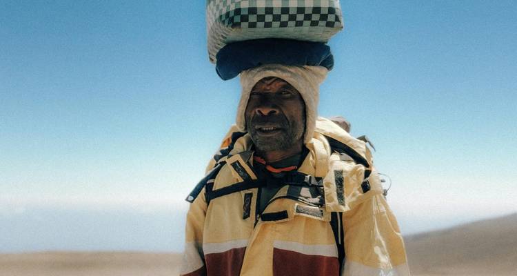 Retrato de un porteador experimentado equilibrando una carga a cuadros sobre su cabeza en el desierto de gran altitud.