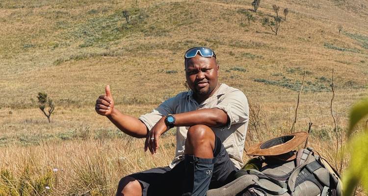 El guía da el visto bueno mientras descansa en las laderas de un páramo cubierto de hierba con su equipo de trekking a su lado.