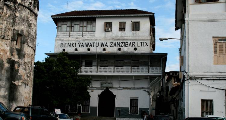 Historisches Steingebäude mit einem Schild "BENKI YA WATU WA ZANZIBAR LTD." gegen einen blauen Himmel.