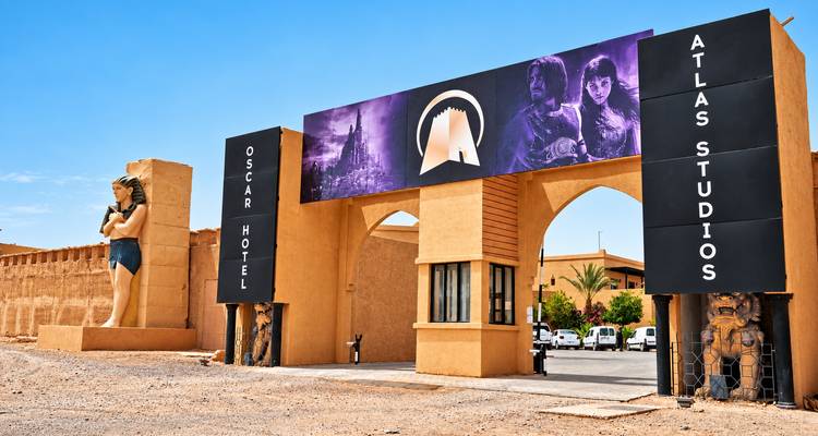 Arco de entrada a Atlas Studios con grandes carteles de películas, flanqueado por una estatua de estilo egipcio en el desierto.