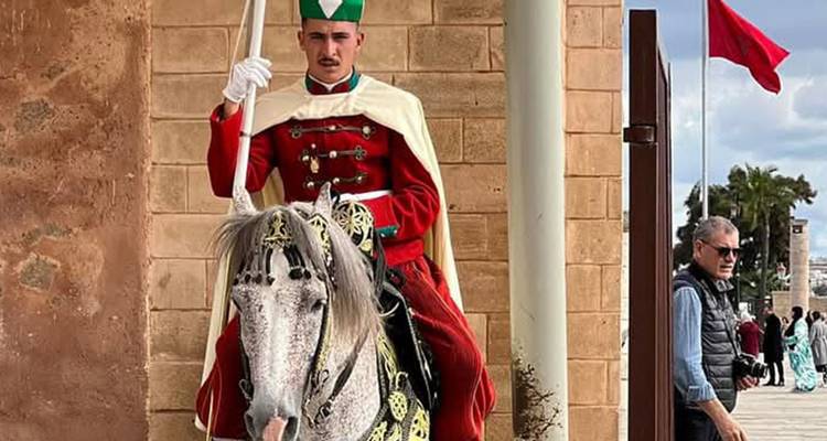 Uniforme bereden wacht in sierlijke rode uitrusting die een speer vasthoudt bij een historische Marokkaanse poort.