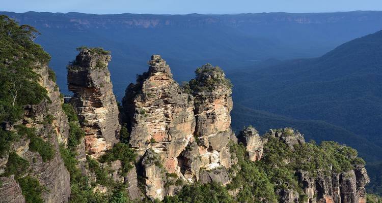 Rugged sandstone spires of the Three Sisters rise above a vast forested Blue Mountains valley.