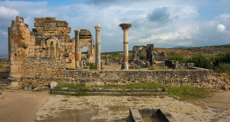 Des ruines de pierre romaines antiques et des colonnes debout sur un site archéologique en haut d'une colline sous des ciels partiellement nuageux.
