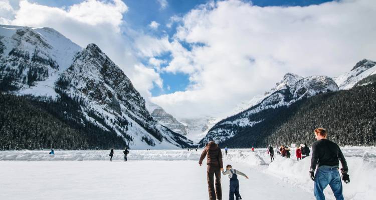 Les skieurs et les familles profitent d'une patinoire extérieure sur un lac gelé entouré de sommets enneigés imposants et de ciels bleus.