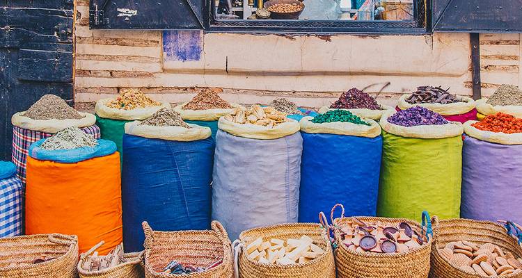 Des rangées de sacs d'épices colorés et de paniers tissés exposés à l'extérieur d'une boutique marocaine.