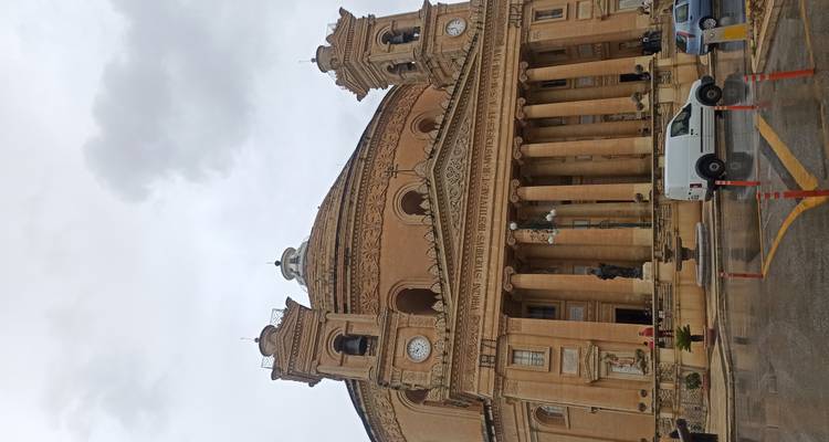 Ronde neoklassieke kerk met twee klokkentorens en zuilen onder regenachtige hemel.