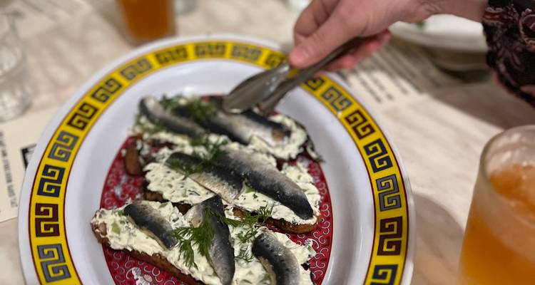 Main plaçant des pinces à salade au-dessus d'une assiette appétissante de pain de seigle garni d'une généreuse couche de crème à l'aneth et de sardines.