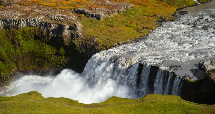 La large cascade s'élance sur une corniche de lave couverte de mousse vers la rivière turbulente en contrebas.