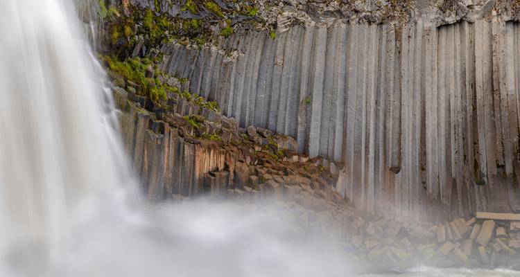 Vue rapprochée de colonnes de basalte verticales à côté des embruns brumeux d'une cascade.