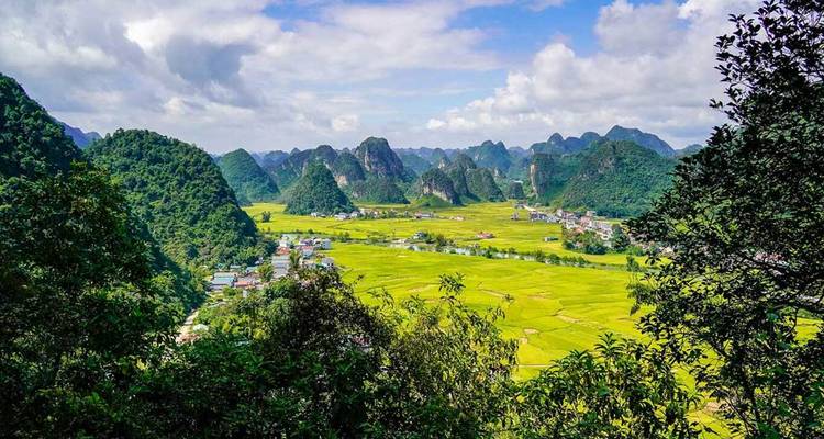 Vue panoramique de champs de riz vert vif et de collines calcaires déchiquetées sous des ciels partiellement nuageux dans le nord du Vietnam.