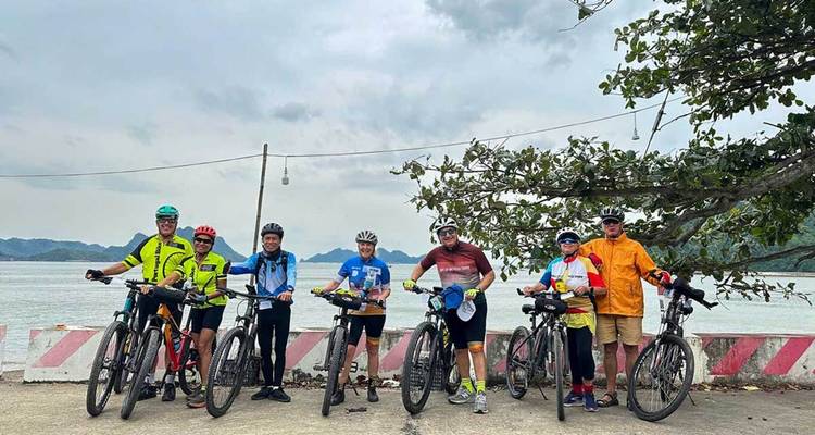Groupe de cyclistes posant avec des vélos chargés à côté d'une baie sous un ciel nuageux.