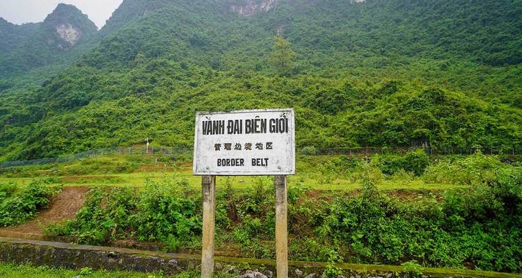 Panneau de ceinture frontalière usé en vietnamien se dressant devant de denses collines de calcaire verdoyantes.