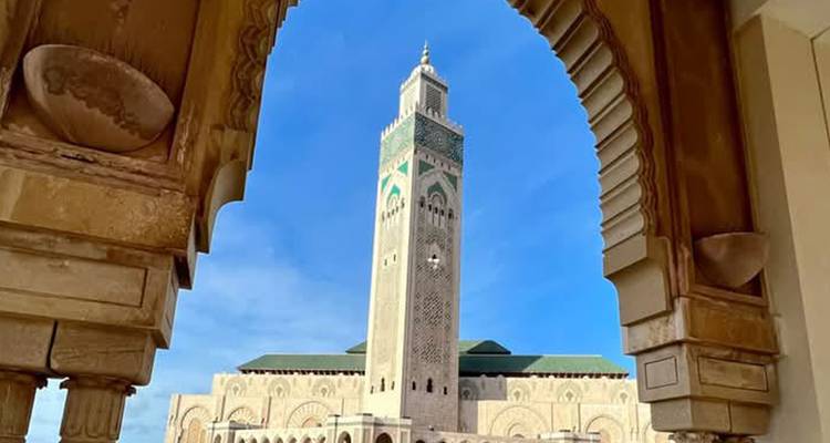 Minaret de la Mosquée Hassan II encadré par une arche en pierre ornementale sur fond de ciel bleu dégagé