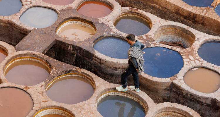 Un homme en équilibre sur le bord de bassins de teinture circulaires dans une tannerie traditionnelle remplie de liquides colorés