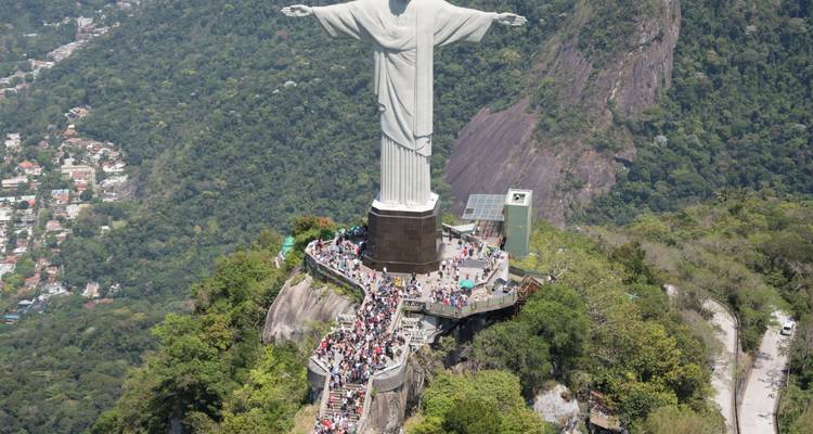 Une vue aérienne du Christ Rédempteur dominant Rio de Janeiro avec des foules sur la plateforme et une forêt luxuriante en dessous.