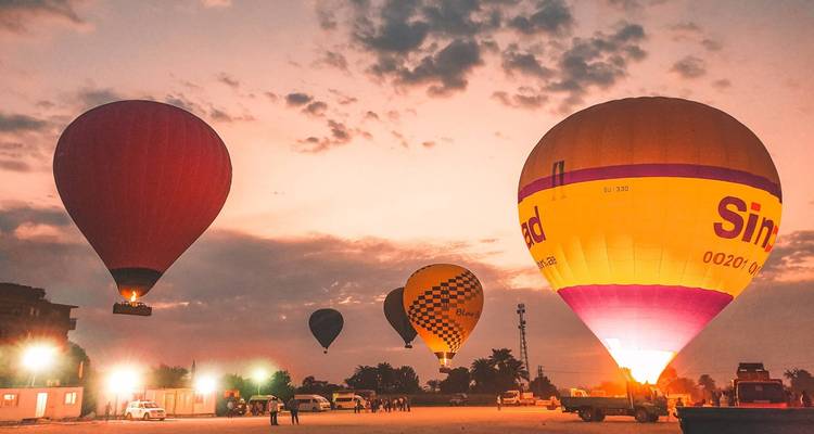 Illuminated hot-air balloons preparing for flight at dawn with a pink-orange sky overhead.
