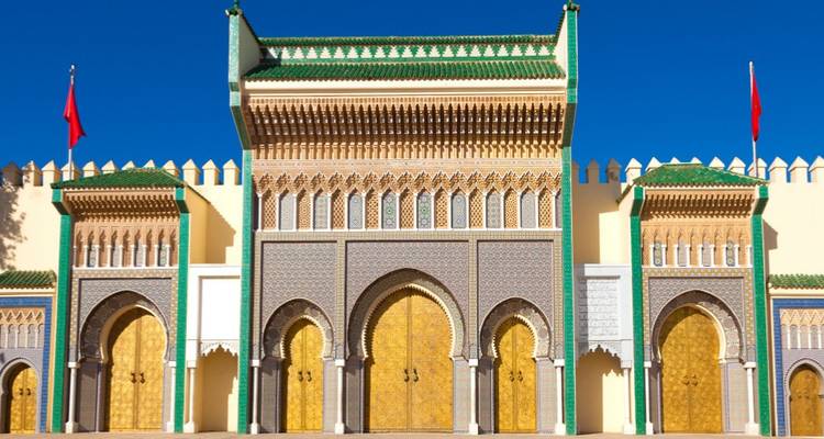 Las grandes puertas doradas del Palacio Real de Fez brillando contra un cielo azul sin nubes.