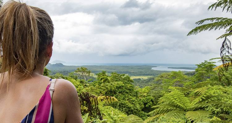 Une femme admire la vaste étendue de la forêt tropicale qui s'étend jusqu'à la ligne de côte et l'océan sous un ciel nuageux.