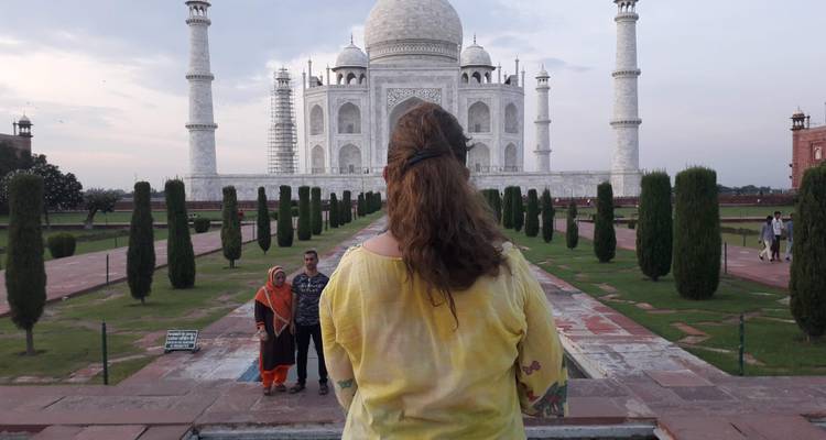 Eine Frau blickt auf das Taj Mahal, während zwei lokale Besucher vor ihr für ein Foto posieren.