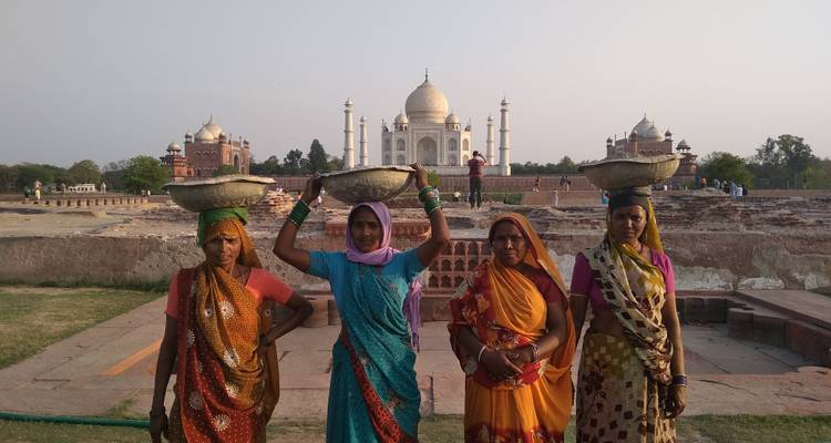 Vier weibliche Arbeiterinnen mit Kopfkörben stehen vor dem Taj Mahal.