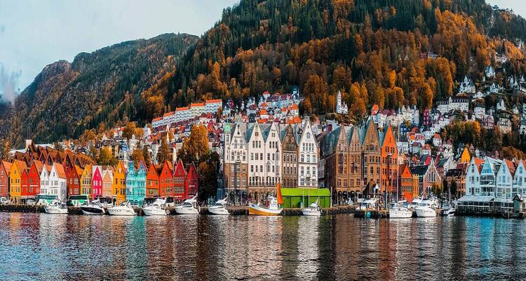 Panorama waterfront du Bryggen de Bergen avec des rangées de maisons en bois colorées se reflétant dans les eaux calmes du fjord.