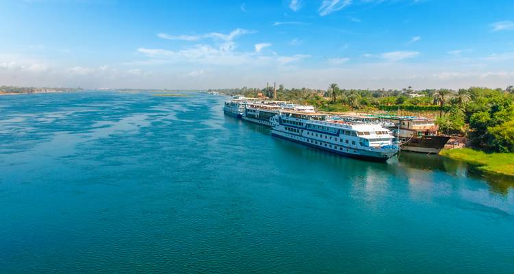 Vista amplia del río Nilo con barcos de crucero atracados bajo un cielo azul brillante