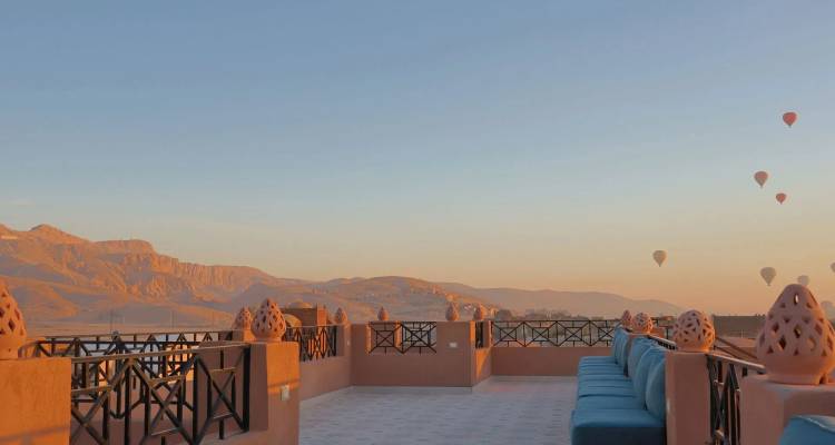 Rooftop terrace at sunrise overlooking desert mountains with scattered hot air balloons in Luxor