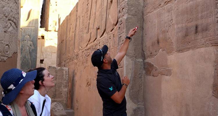 Guide explaining ancient hieroglyphs on temple wall to attentive visitors