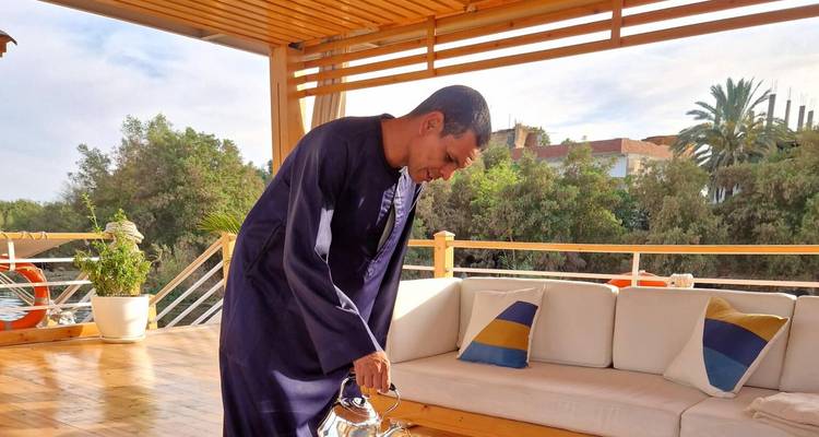 Crew member in traditional galabeya pouring tea on open deck seating area