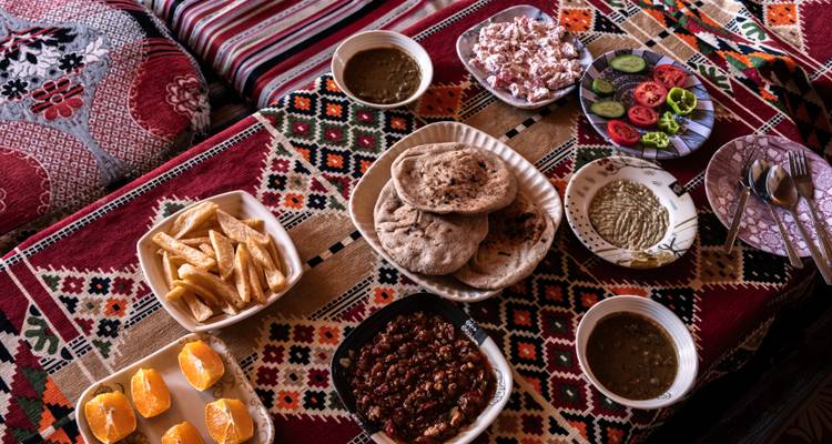 Kleurrijk assortiment van Egyptische gerechten, waaronder flatbreads, stoofschotels, friet en verse salades op gemusterde textiel.