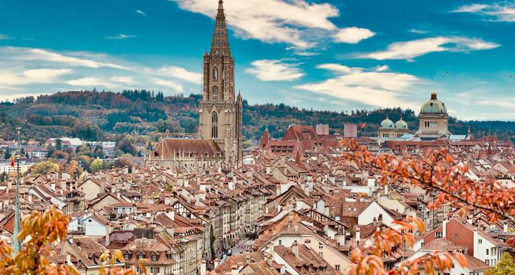Vista panorámica de Berna con la aguja de la catedral elevándose sobre tejados de terracota y árboles otoñales