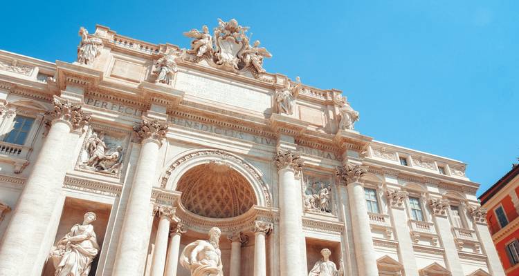 Ornate marble facade and statues of the Trevi Fountain shining under a clear blue sky