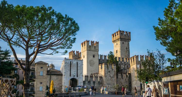 Castillo medieval Scaliger en Sirmione con torres de piedra almenadas y un puente lleno de visitantes bajo un cielo azul despejado.