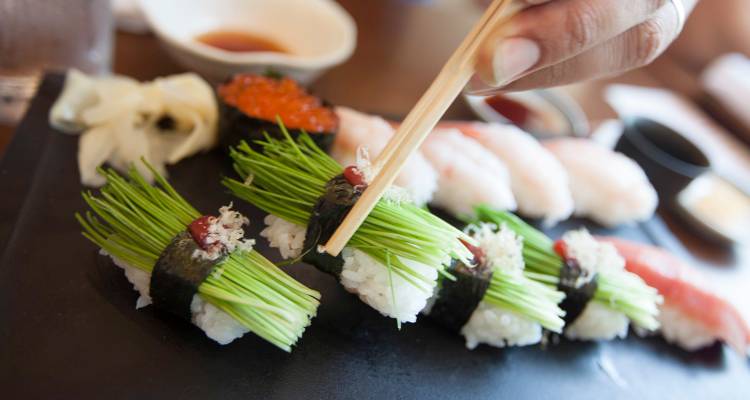 Une main utilisant des baguettes arrange des makis créatifs garnis de ciboulette fraîche et d'œufs de poisson.