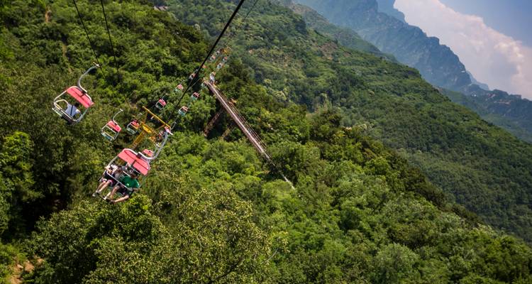 Teleférico al aire libre llevando visitantes sobre montañas verdes cerca de la Gran Muralla