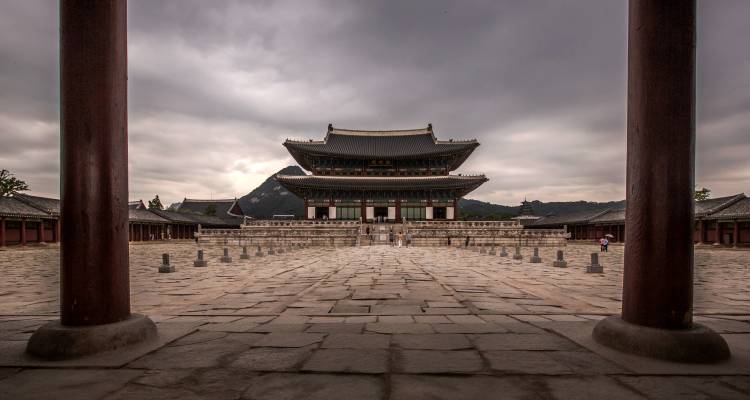 Vue symétrique de la cour du Palais Gyeongbokgung encadrée par des piliers en bois sous un ciel nuageux.