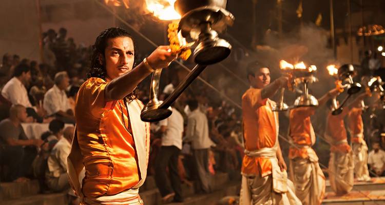 Sacerdotes con atuendos naranjas realizan el ritual ardiente de Ganga Aarti con lámparas de latón levantadas ante una multitud en los ghats de Varanasi.