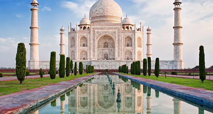 Vista clásica y simétrica del Taj Mahal con estanque de reflexión, jardines y cielo azul despejado.