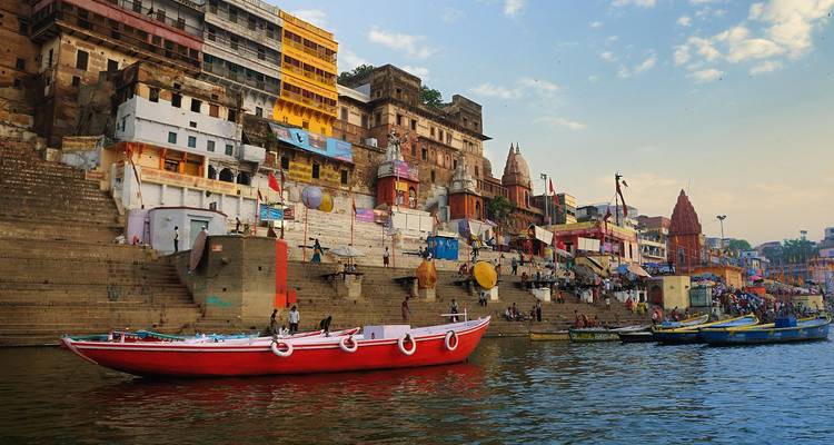 Los coloridos ghats de la orilla del río en Varanasi con templos, edificios apilados y botes flotando en el Ganges al amanecer.