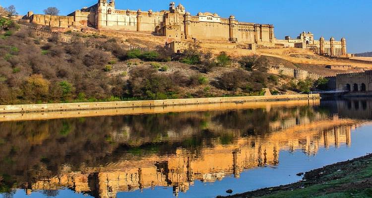 Amber Fort badend in gouden ochtendlicht met een perfecte weerspiegeling in het stilstaande water van het Maota-meer.